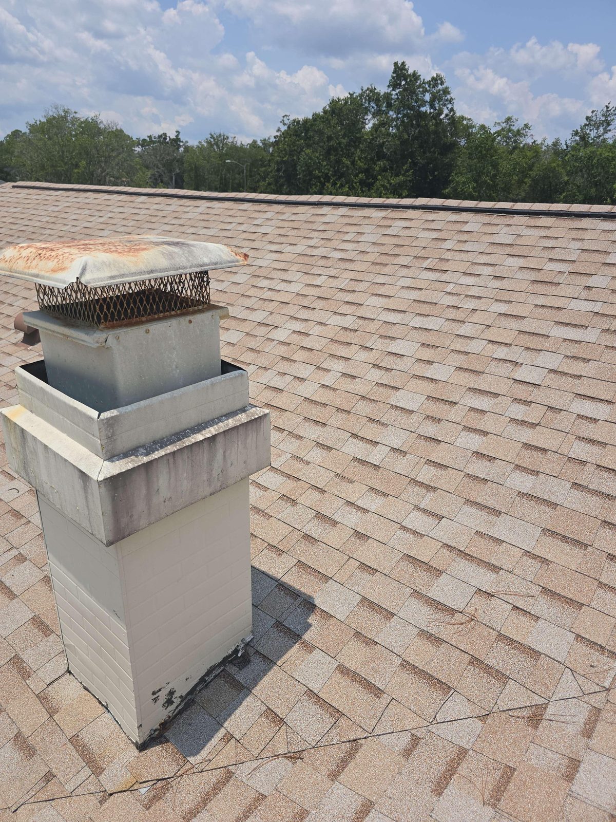 A brick chimney extending through a shingled roof, with the roofline and nearby roof surfaces visible around it