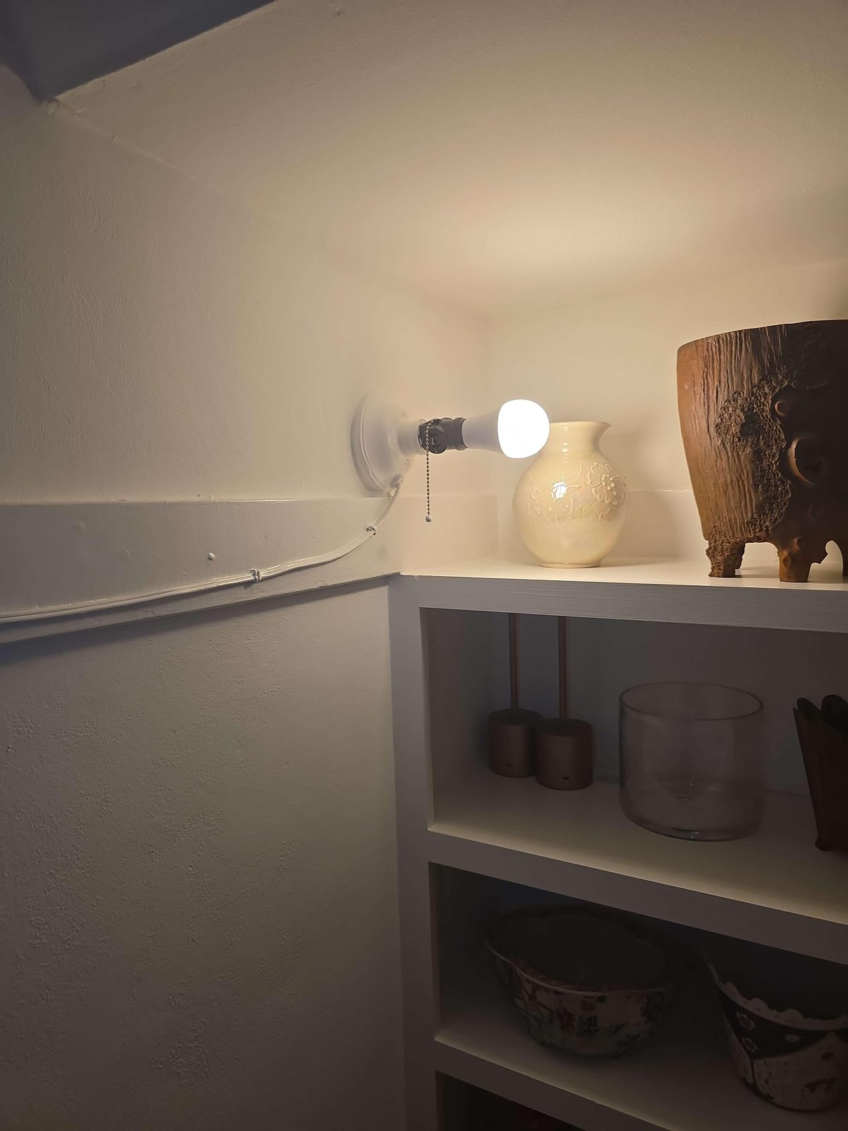A bare light fixture mounted in a closet ceiling, positioned directly adjacent to a wooden shelf, with an orange extension cord running visibly between the wall switch and the fixture.