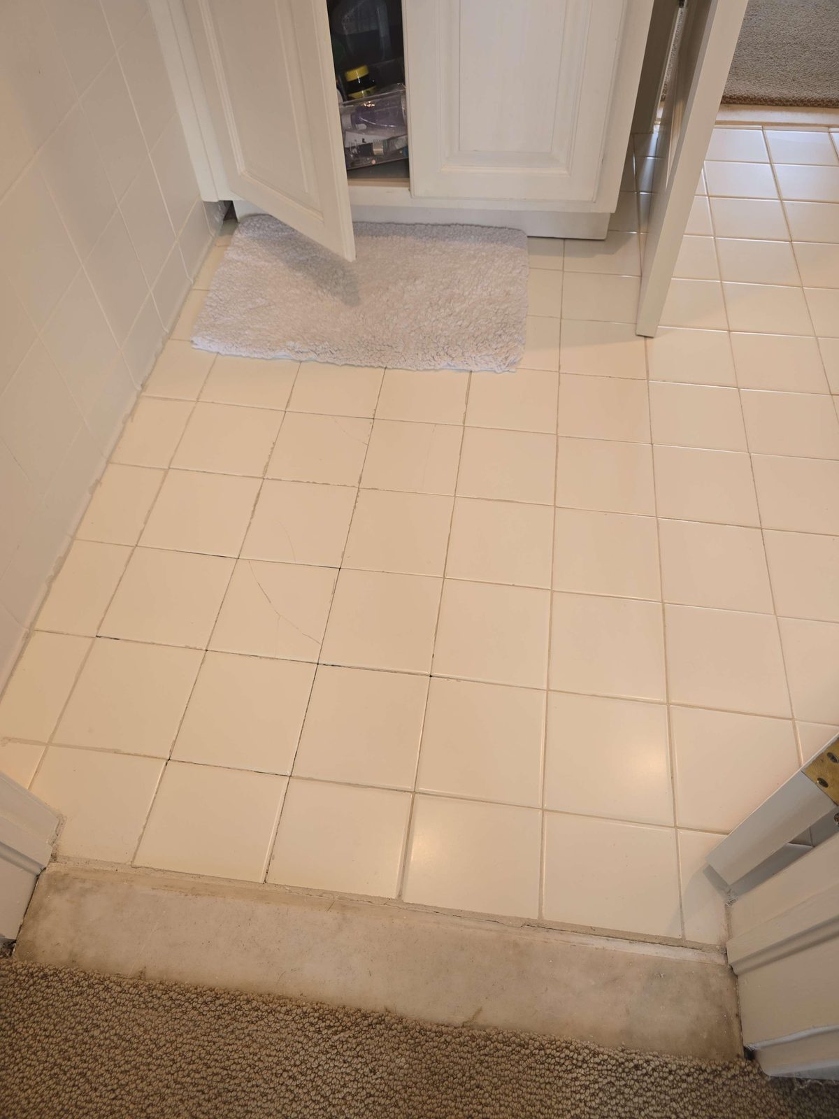 Cracked ceramic floor tiles with open grout joints and a visibly uneven surface in an upstairs bathroom