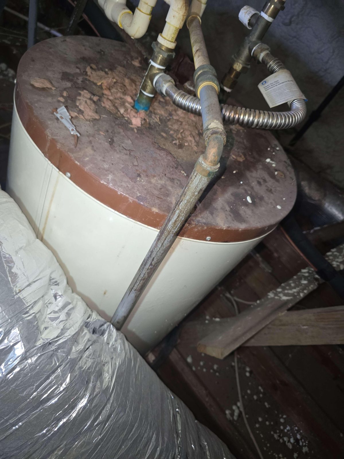 A water heater tank resting in an attic space, with no visible electrical connections attached to the unit