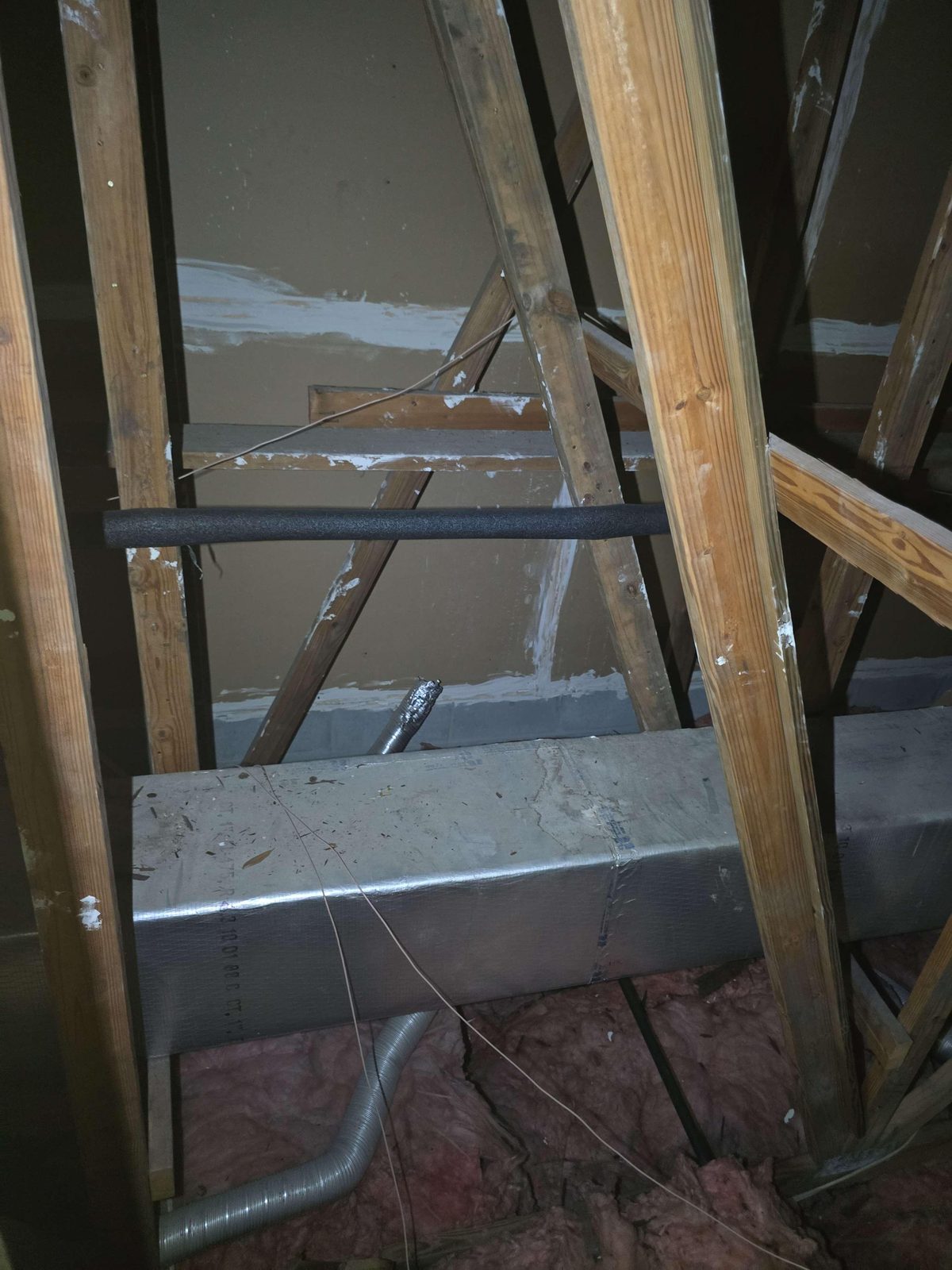 A flexible duct pipe ending inside a dim attic, with no connection to an exterior vent cap or wall opening