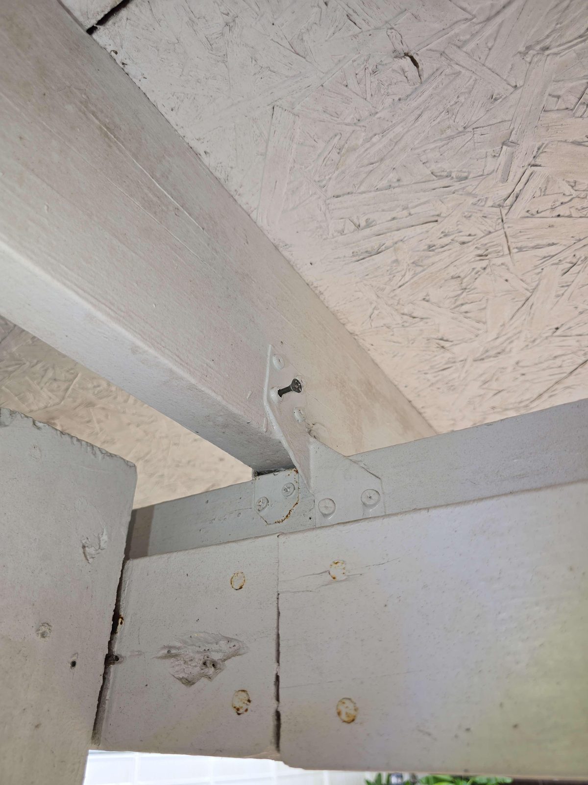 A metal hurricane strap connector bridging a roof rafter and wall framing, with a screw whose narrow shaft is visible at the fastener hole