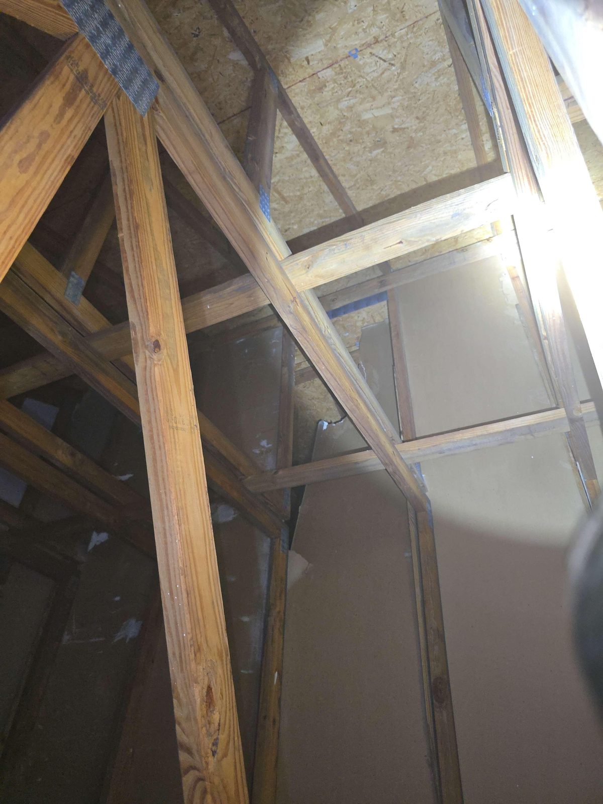 View from inside an attic showing an opening or gap in the wall assembly that separates two attached dwelling units, with framing and insulation visible around the breach