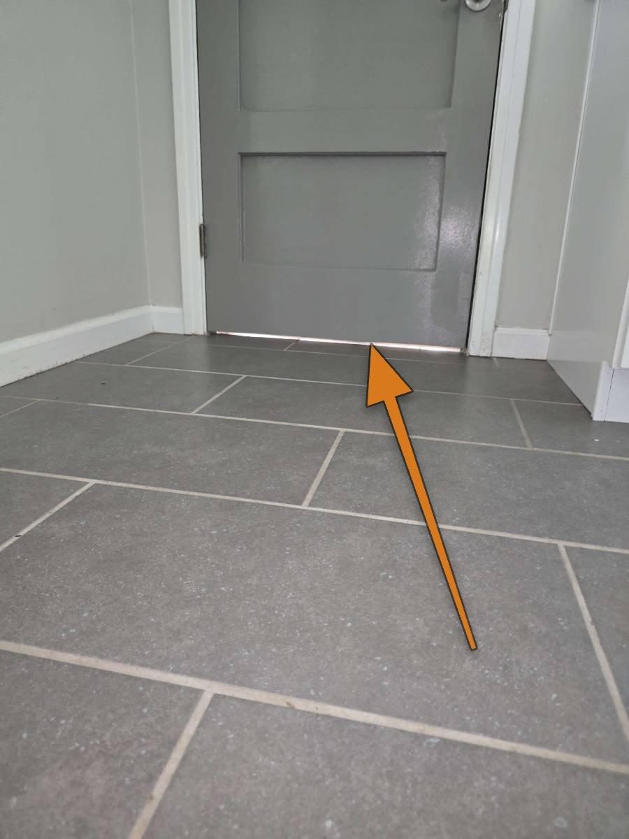 Bottom edge of a door between a garage and living space, showing a gap where a threshold seal would normally sit against the floor