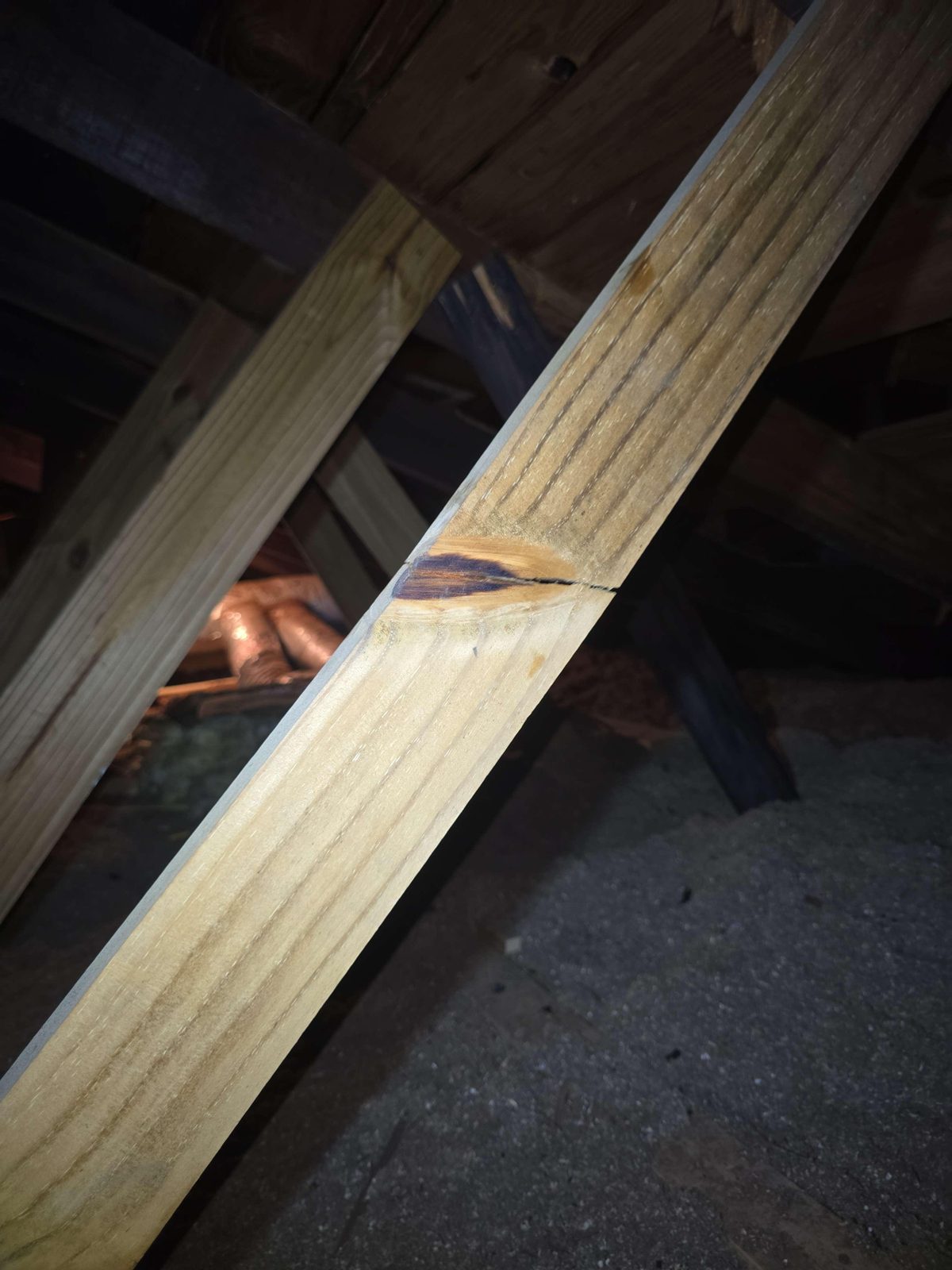 A wooden diagonal brace spanning between roof framing members, showing a visible crack across the middle of the board
