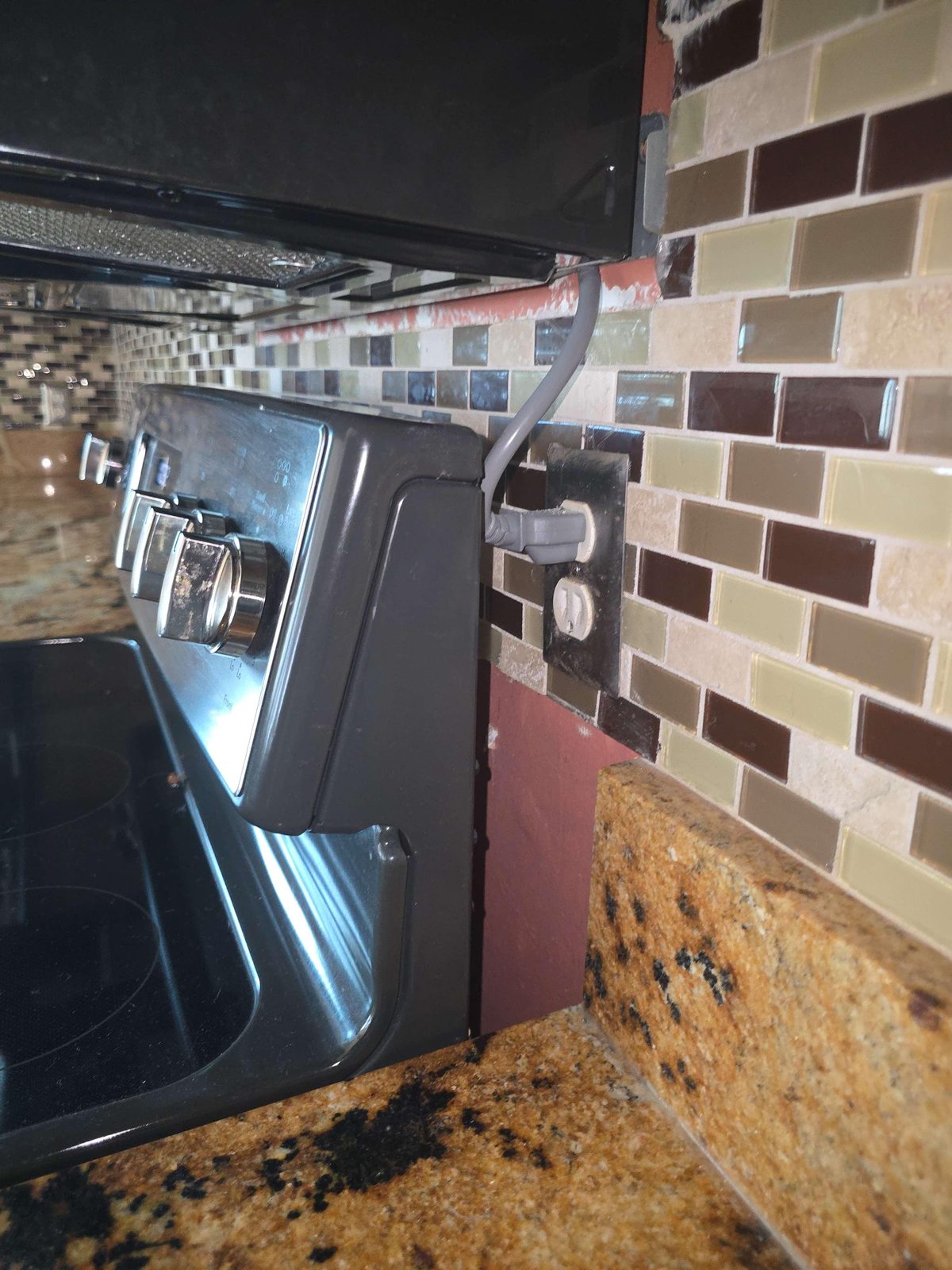 An electrical receptacle outlet partially obscured behind the side of a freestanding kitchen range, with the range pushed back against the wall