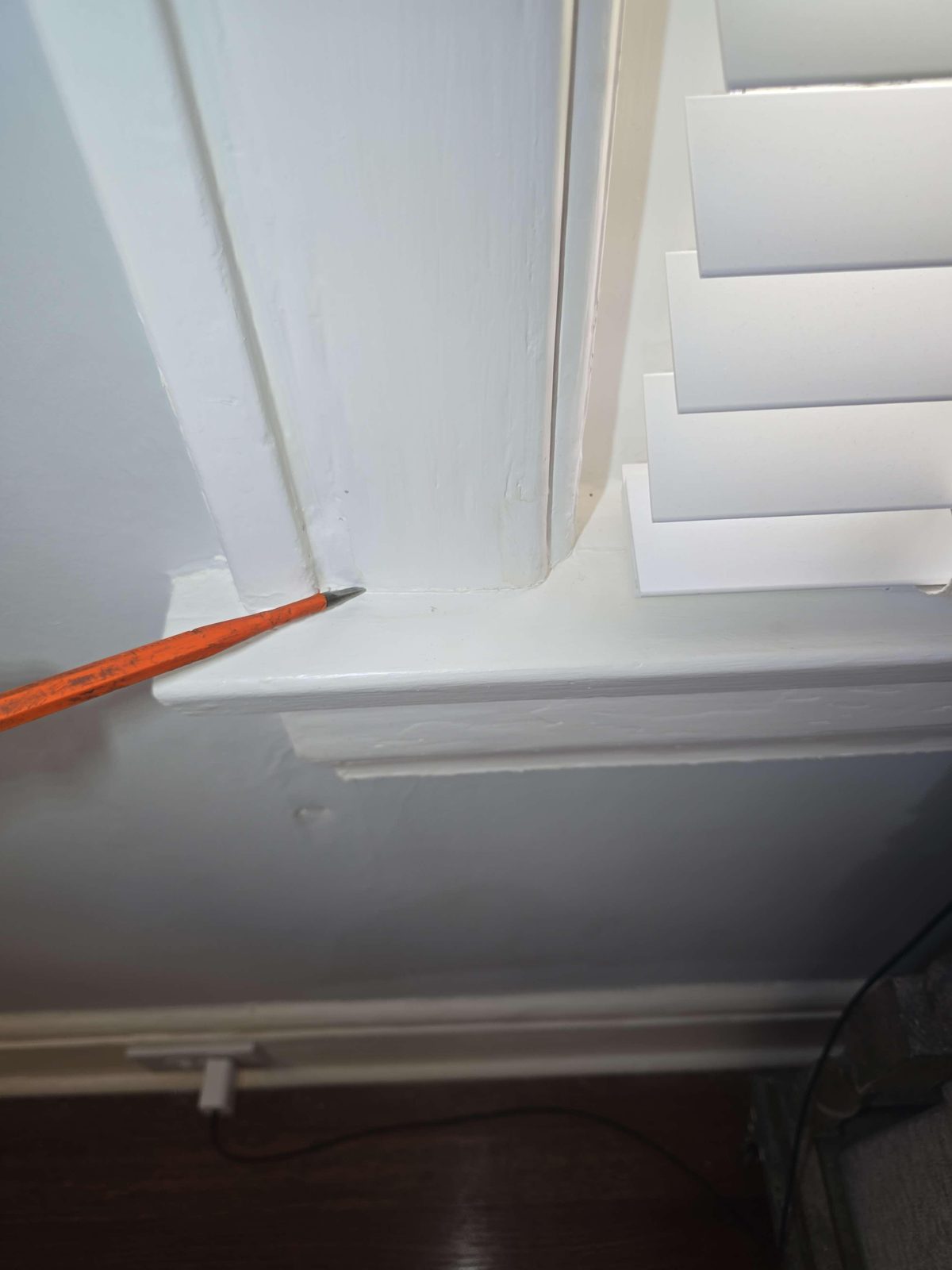 A close-up of a pin-style moisture meter probe pressed into a plaster wall surface where the plaster has crumbled and broken away at the contact point, with vinyl wallpaper peeled back slightly at the edge
