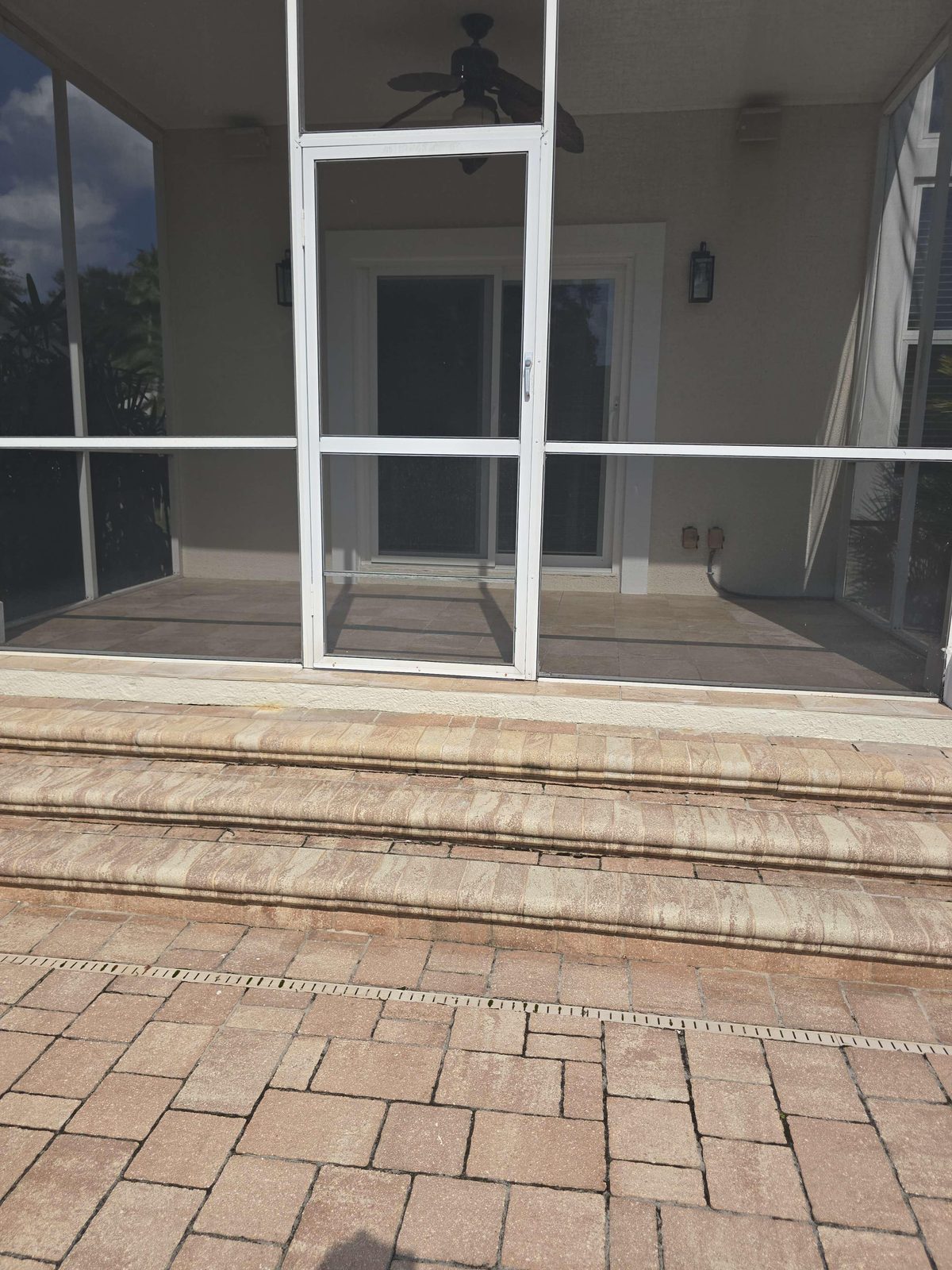 Exterior rear patio steps showing an outward-swinging screen porch door at the top with no landing platform and no handrail along the stair run