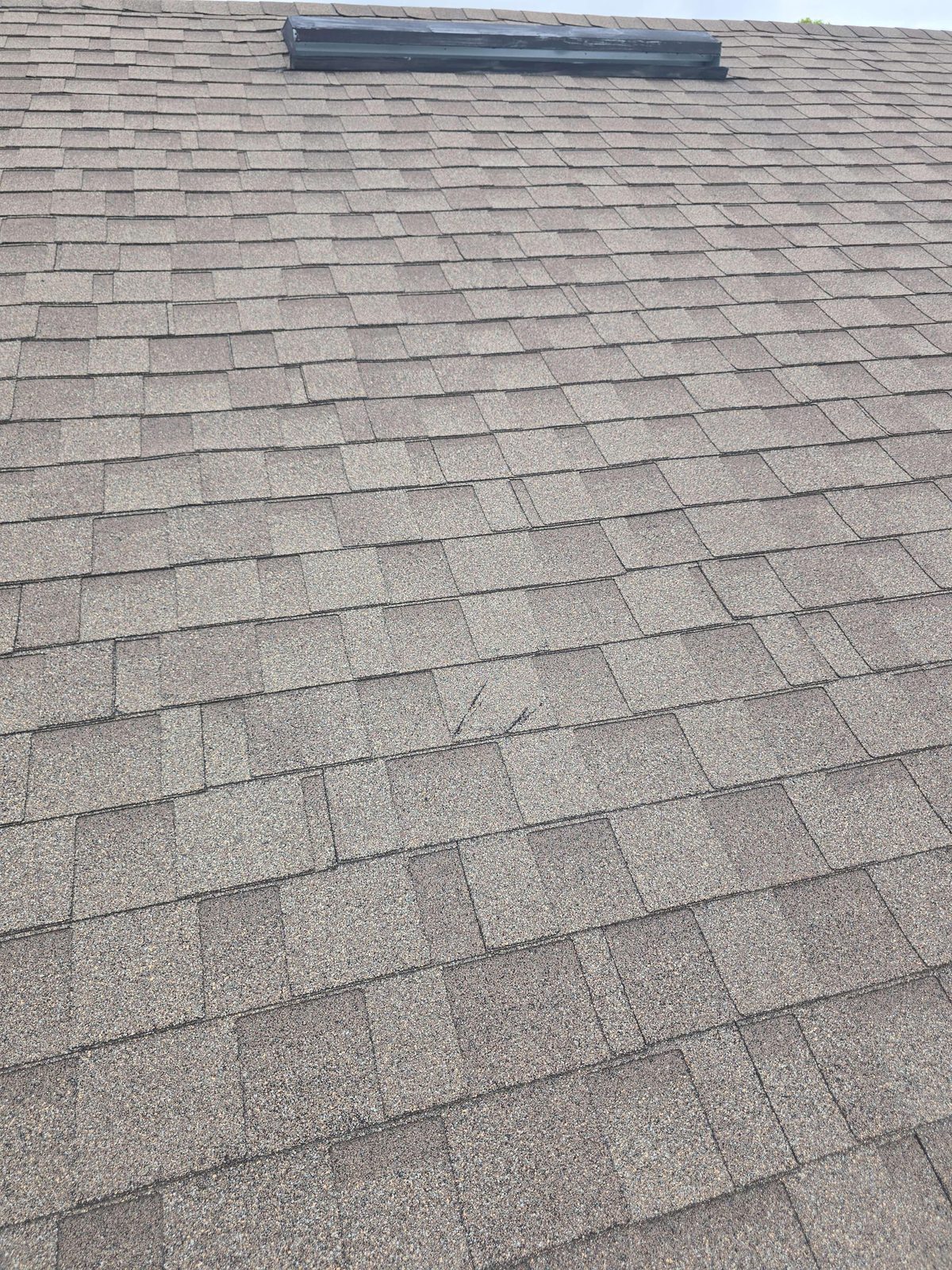 Close-up of asphalt roof shingles showing a localized area of cut or gouge marks through the granule surface at the center of the right-side roof plane
