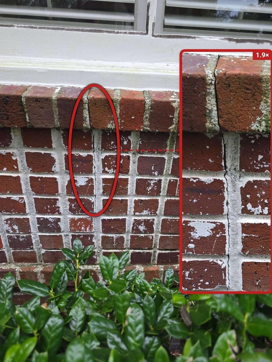 Close-up of stepped cracks following the mortar joints in a brick veneer wall near a window opening, with cracks visibly wide enough to admit a finger edge