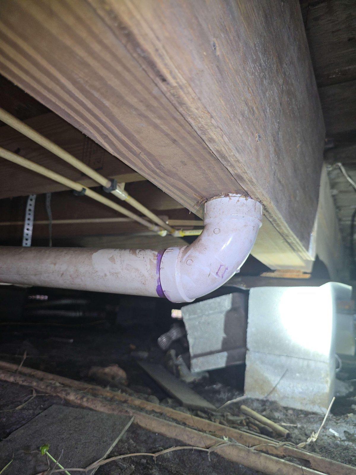A wooden structural beam with a circular hole drilled through it, with a plumbing drain pipe passing through the opening