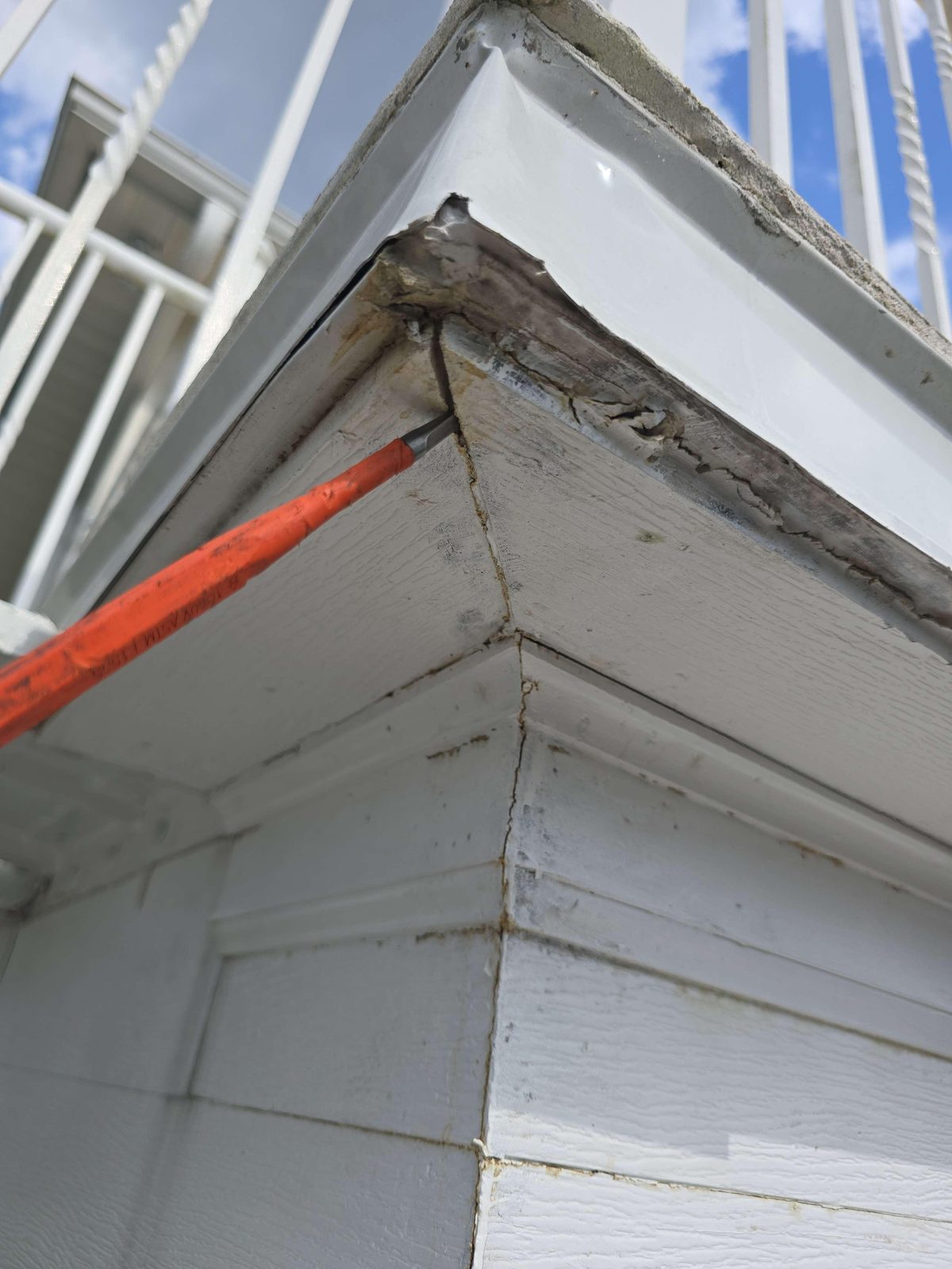 Close-up of exterior trim at a balcony edge showing discoloration, staining, and visible gaps or voids where sections of trim material meet