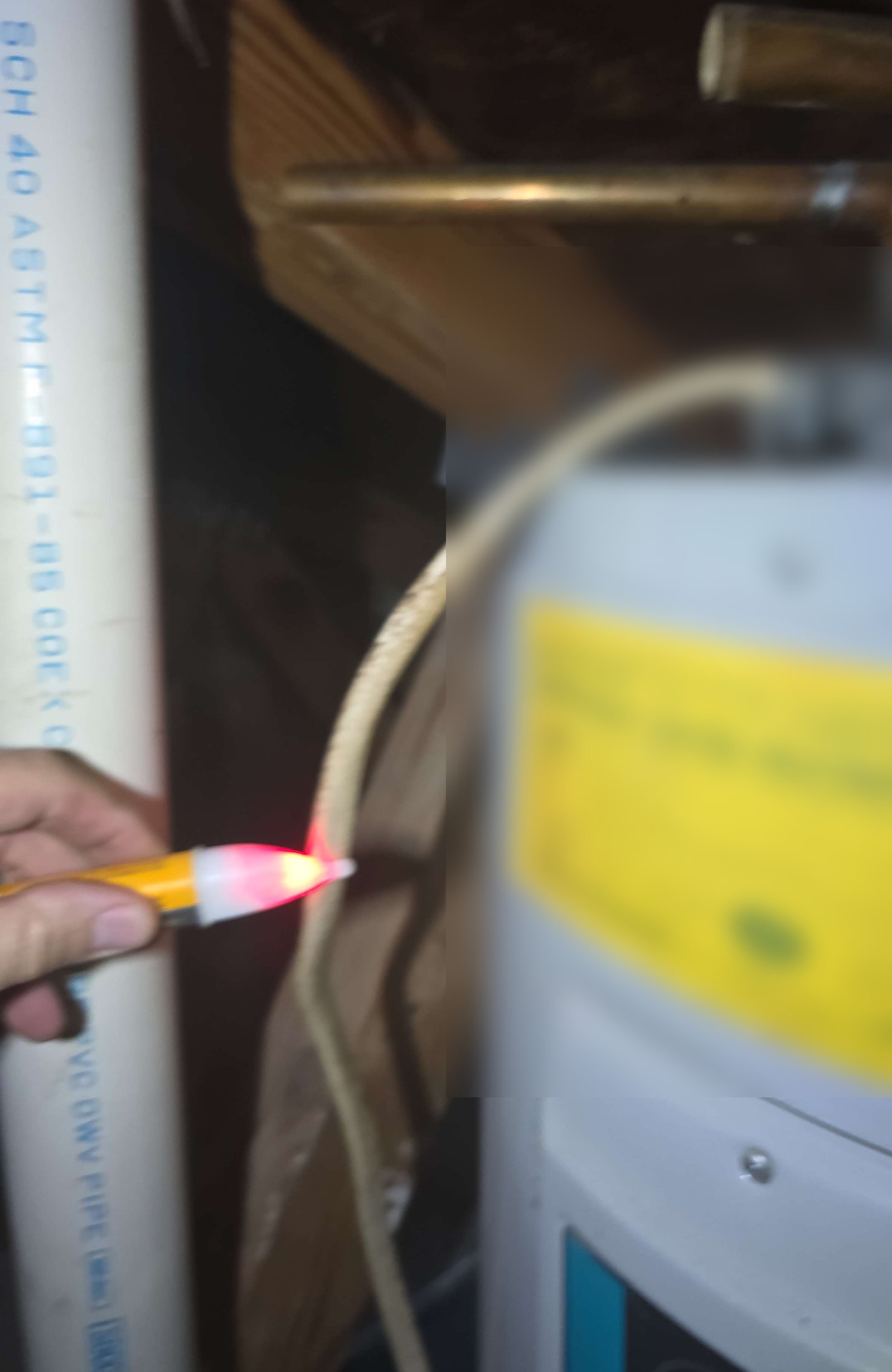 Non-contact voltage tester glowing red against the supply wiring of a water heater in an attic